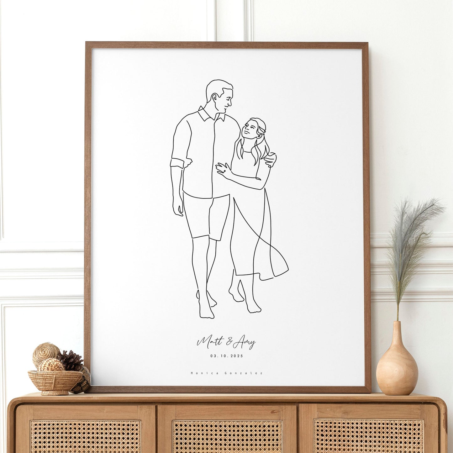 Framed line drawing of a couple on a white wall above a wooden console table.