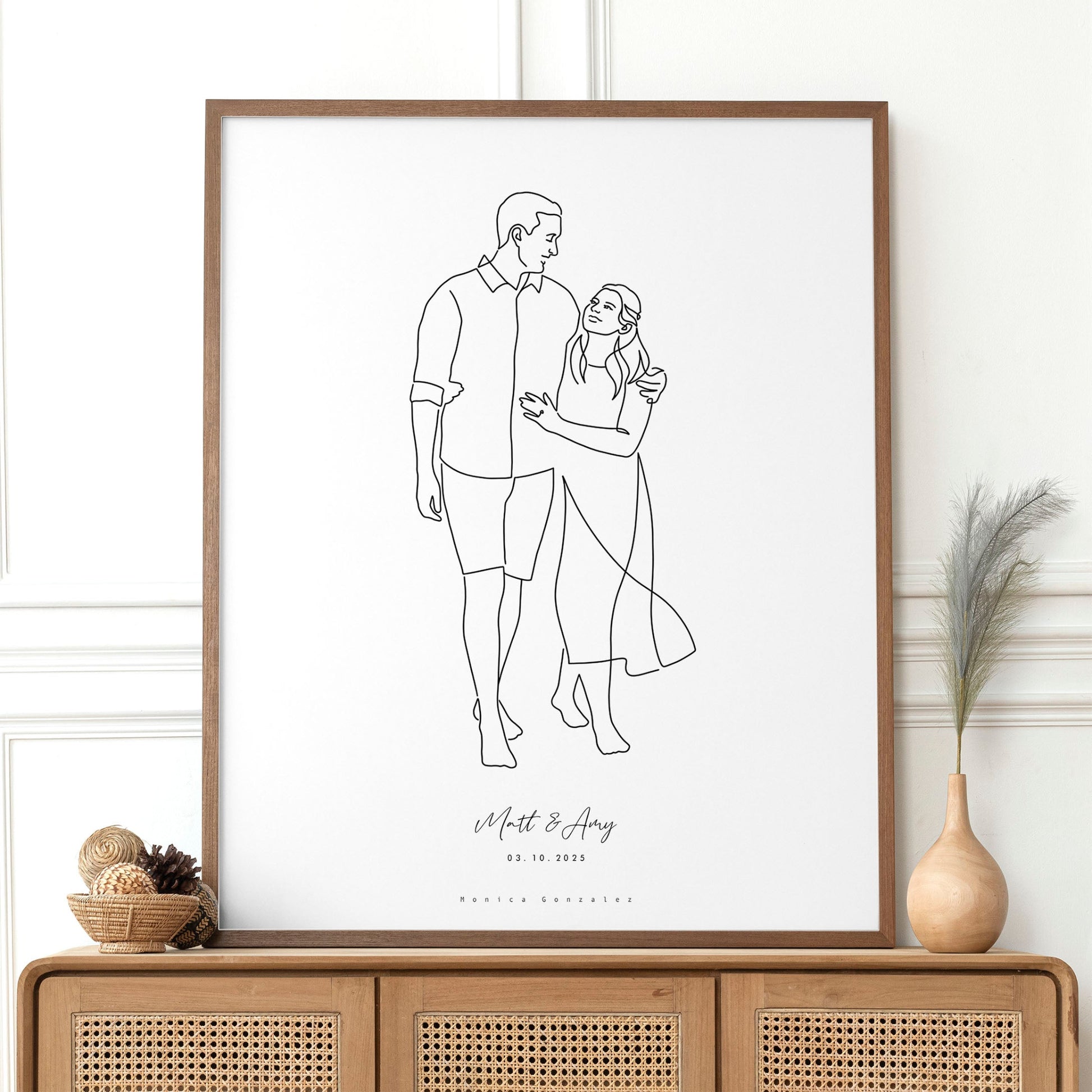 Framed line drawing of a couple on a white wall above a wooden console table.